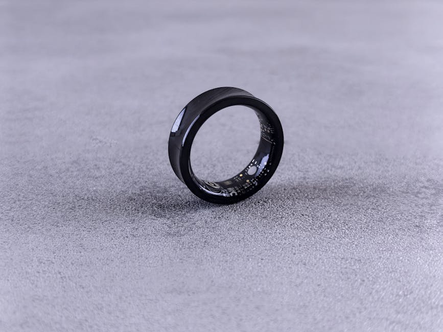 Black smart ring with visible internal circuitry on a textured concrete surface